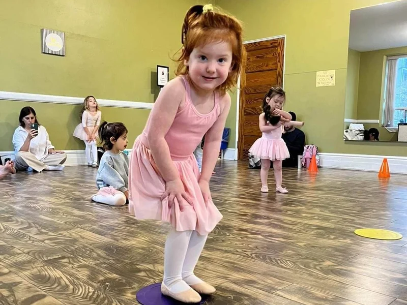 Young girl in pink ballet outfit smiling during an infant dance class in Toronto with caregivers watching