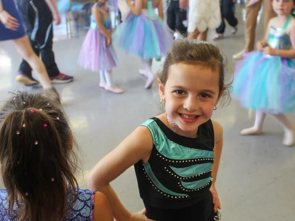 A happy young girl in a teal and black recital outfit participating in infant dance classes with other students in tutus.